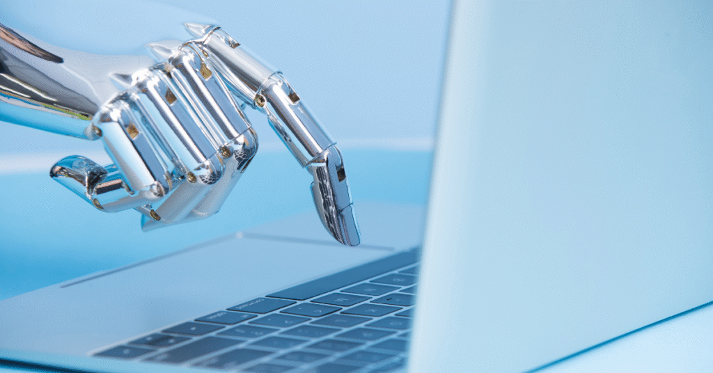 Close-up of a chrome robotic hand typing on a laptop keyboard, symbolizing artificial intelligence and automation in technology