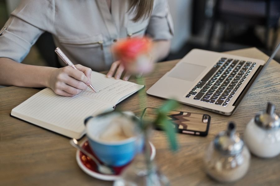 image of woman writing at desk with computer in front her her