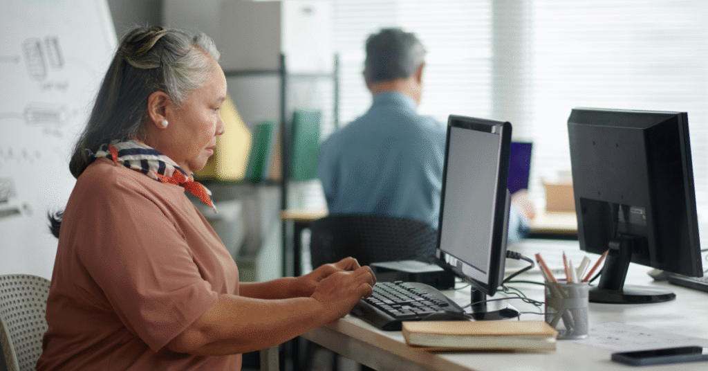 Older woman sitting at a desk typing on a computer in a bright, professional office setting