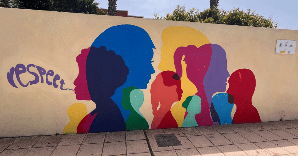 Colorful mural of overlapping human silhouettes in bright shades of blue, red, yellow, green, and purple. The word ‘respect’ flows from one figure’s mouth, symbolizing inclusivity and dignity.