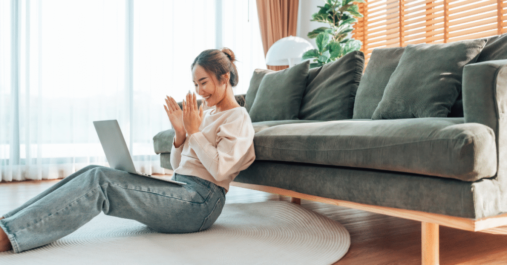 Young woman smiling while working on a laptop in a bright, modern living room, representing productivity and digital marketing success through effective website design.