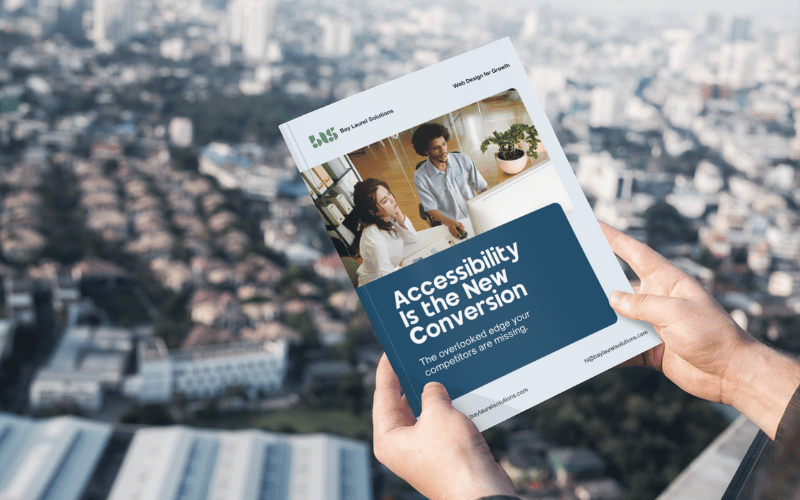 Hands holding a booklet titled 'Accessibility Is the New Conversion' against a blurred aerial view of San Francisco, California.