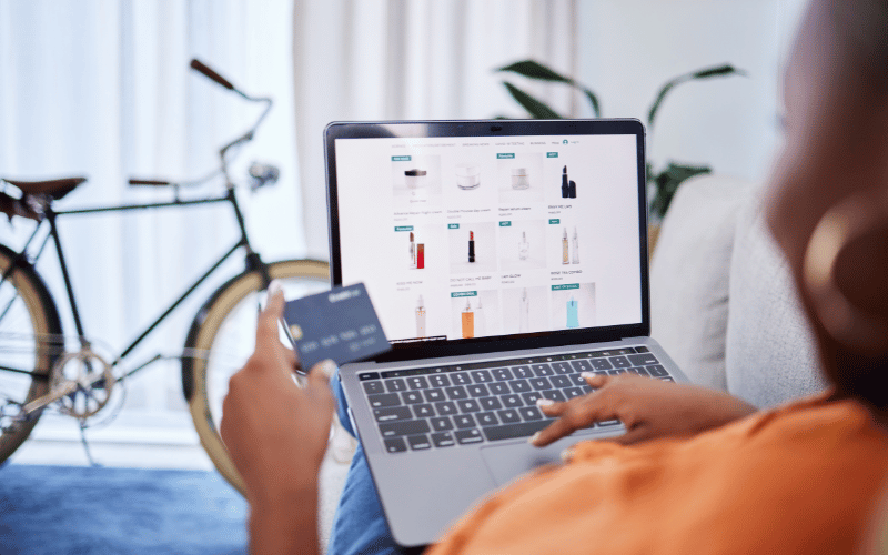 Person holding a credit card and browsing products on a laptop screen in a living room.