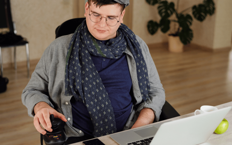 Person using an adaptive mouse while working on a laptop at a desk.