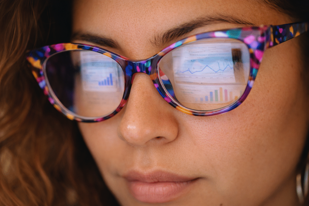 Close-up of woman wearing bright yellow glasses with analytics dashboard reflected in lenses
