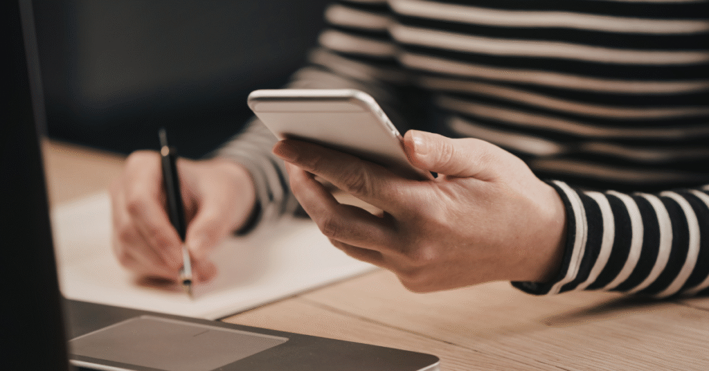 Person taking notes while reviewing website content on a smartphone