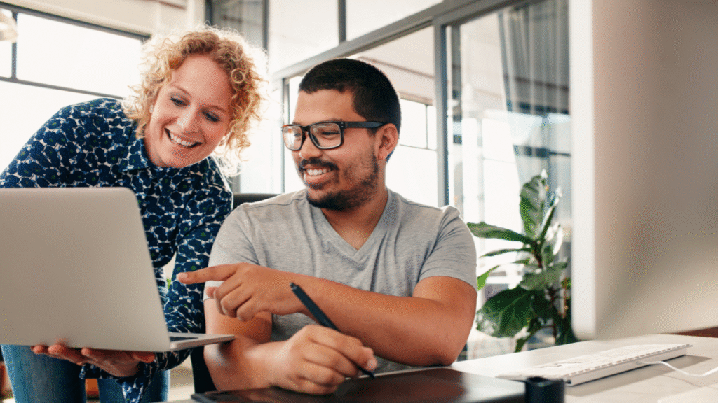 Two people collaborating while reviewing a website or digital project on a laptop in an office.